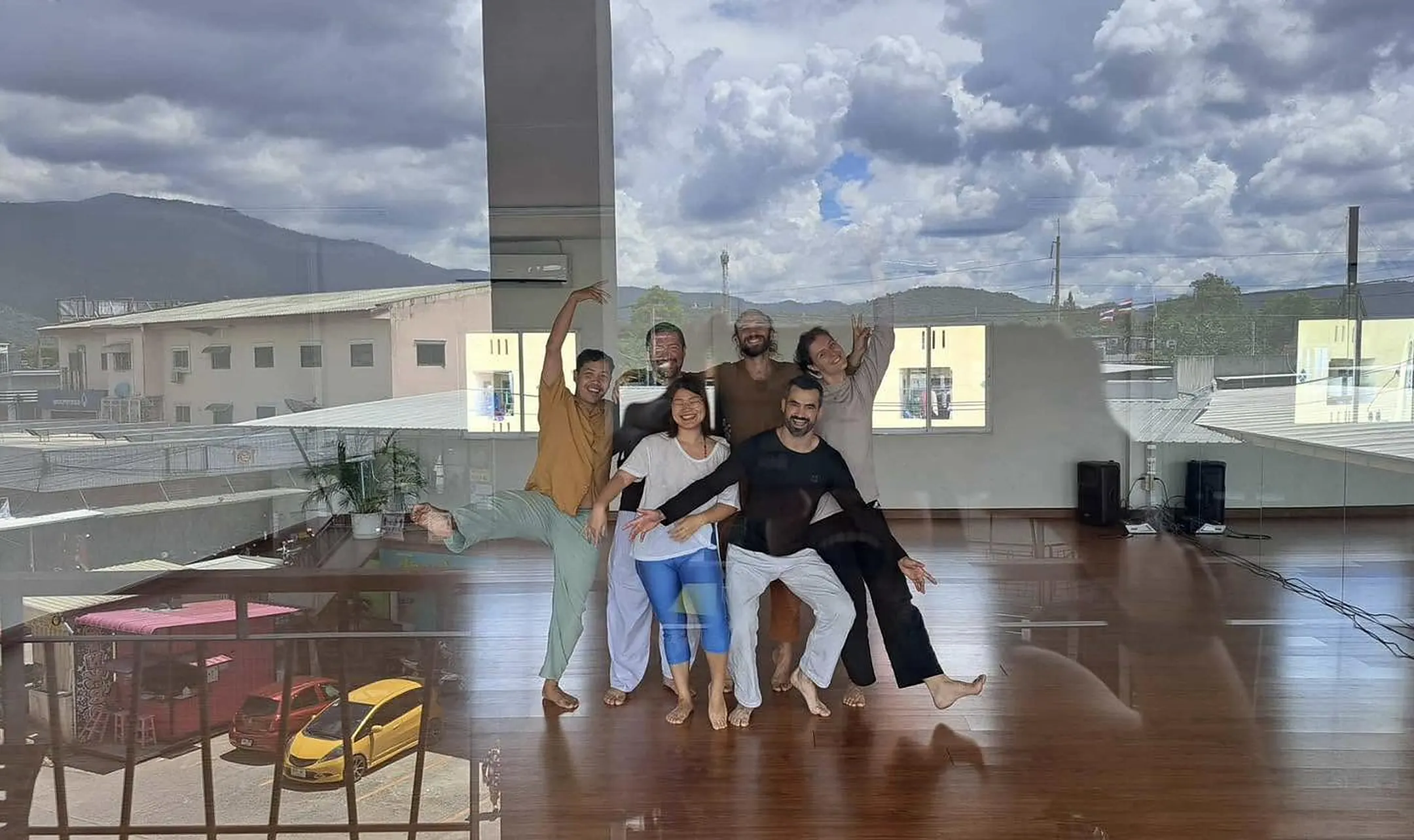Six movers laughing and posing together on the studio floor, reflected in the glass with the mountains behind