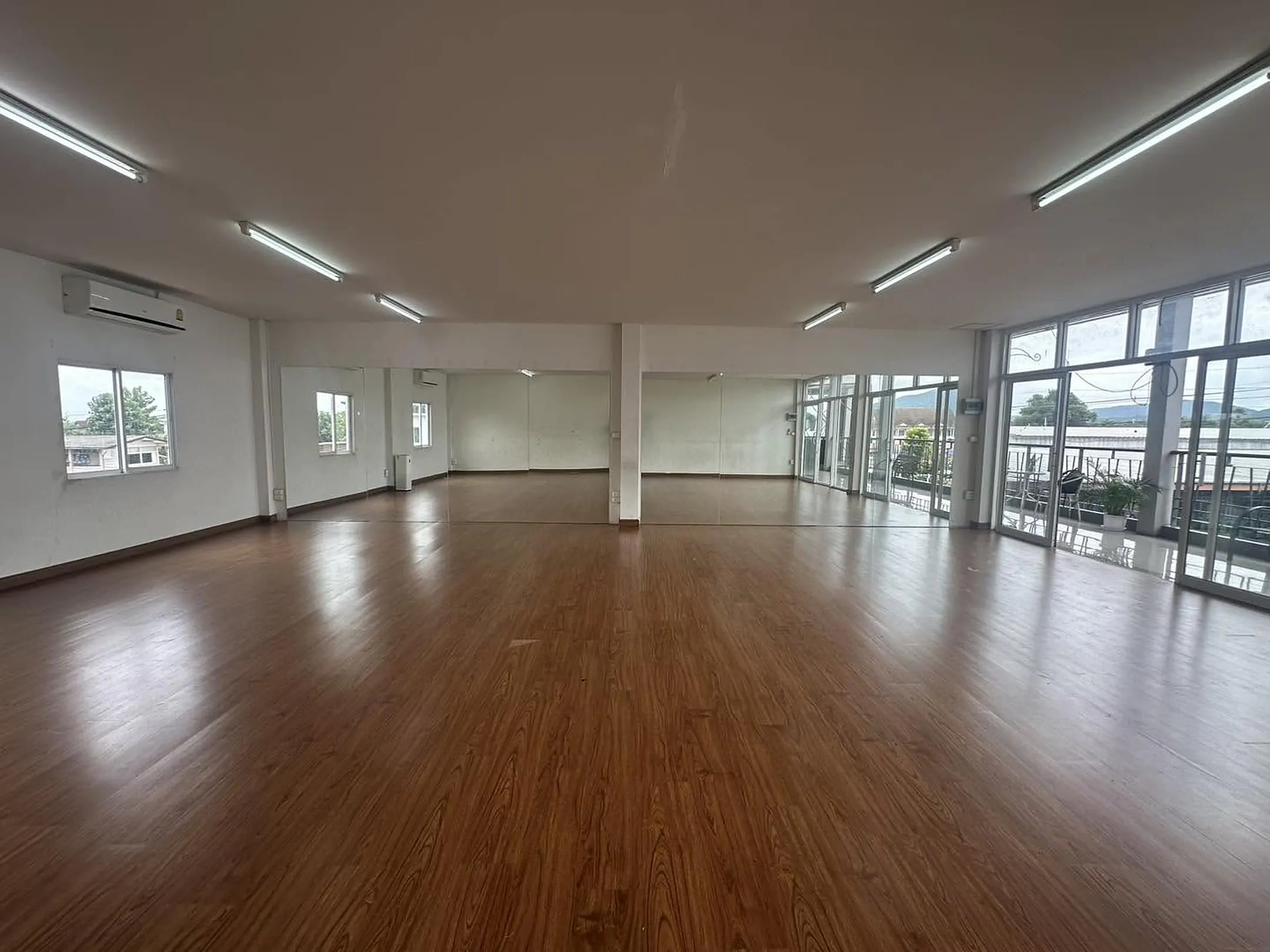 The empty studio with a warm wooden floor, a full mirrored wall and glass doors opening to a balcony with mountain views